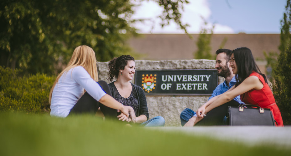 Students sitting outside Exeter sign on Streatham campus