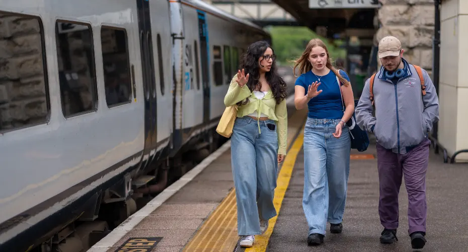 A group of three students walking along the platform at a train station.