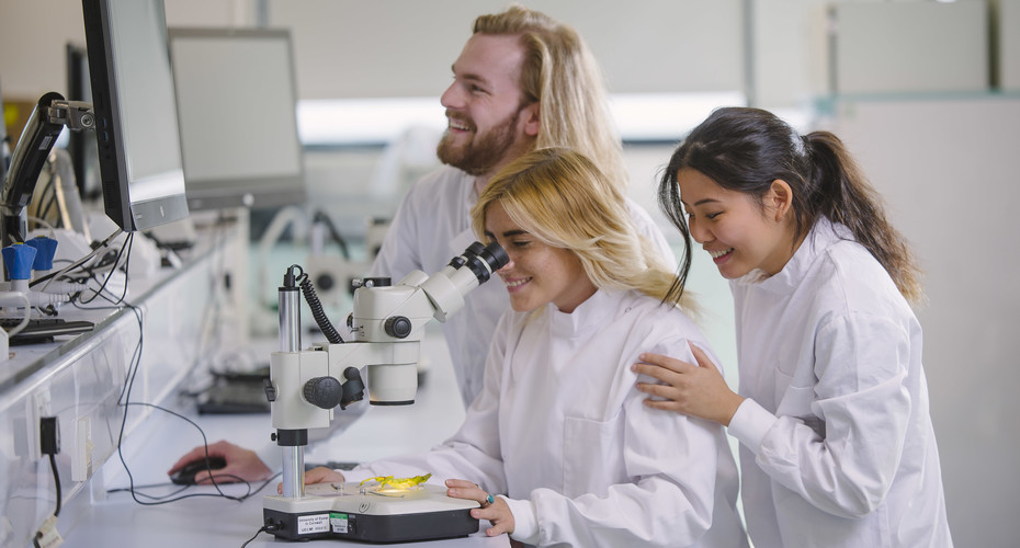 Three Biosciences students working with a microscope in a lab