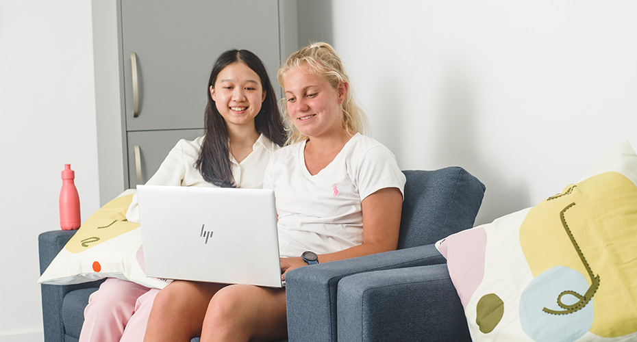 two students on blue sofas looking at silver laptop