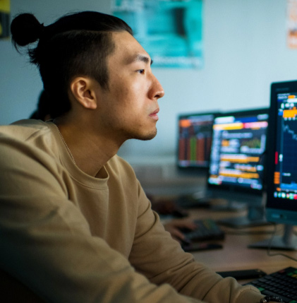 A man sitting at a desk with multiple computer screens, working diligently on various tasks.