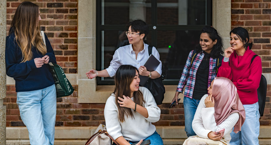 5 students chatting and laughing on the steps at the business school courtyard.
