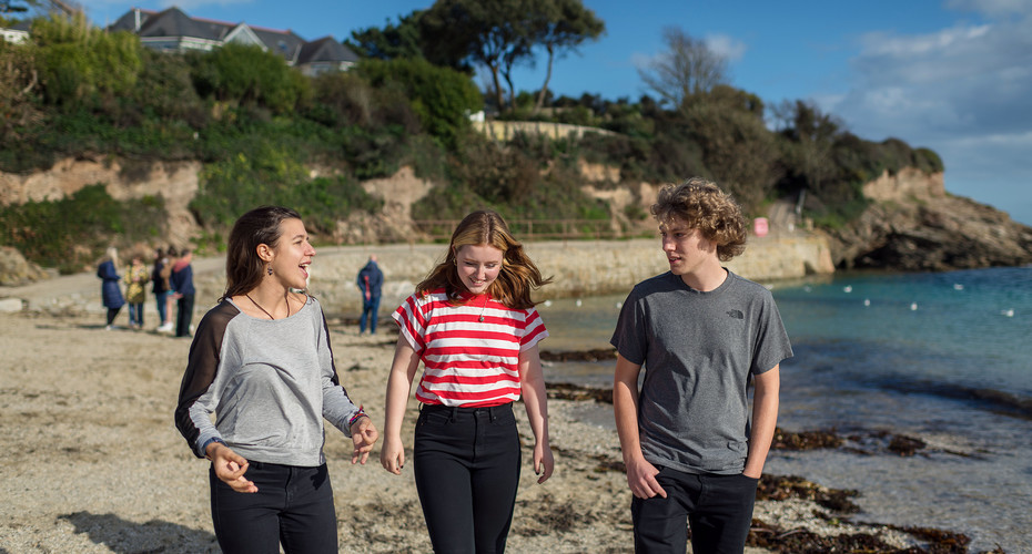 Three young individuals stroll along the beach, enjoying the sun and the sound of the waves.